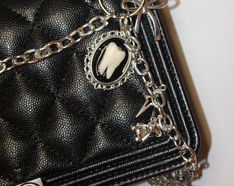 May include: A black quilted handbag with a silver chain strap and multiple charms, including a tooth charm, a cross charm, and a bow charm.