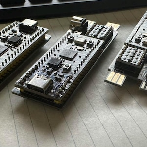 May include: Four rectangular black printed circuit boards arranged in a row. Each board features various electronic components, including microchips, silver-colored ports, and gold-plated connector pins at one end, all mounted on a dark base.