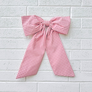 May include: A large pink and white gingham bow with long tails. The bow is tied in a knot and the tails are hanging down.