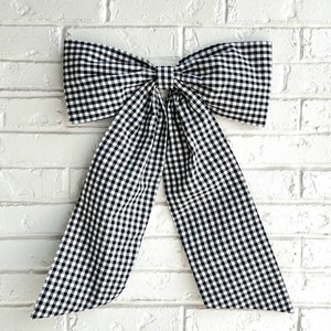 May include: A large black and white gingham bow, tied with a loop and tails, against a white brick wall background.