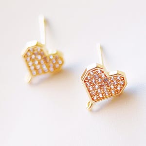 May include: A pair of gold heart-shaped earrings with clear cubic zirconia stones.