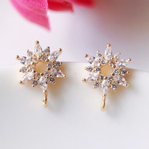 May include: A pair of gold earrings with a starburst design. Each earring features a circle of small, clear stones surrounded by larger, clear stones.