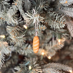 May include: A brown and white ceramic ornament shaped like a loaf of bread hanging on a Christmas tree.