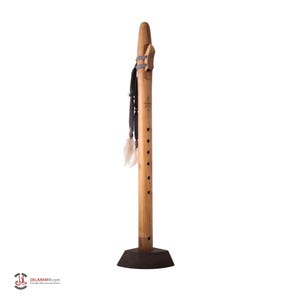 May include: A wooden Native American flute with a dark brown base. The flute is light brown with several finger holes and decorative accents, including a leather strap and feathers. The flute is standing upright.
