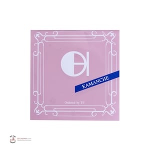 May include: A pink square with a white ornate border. The centre of the square features a white circle with a black line through it. The text "KAMANCHE" is printed in blue on a white ribbon. The text "Ordered by TF" is printed in black below the ribbon.