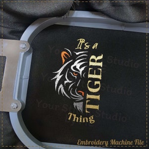 May include: Embroidery machine file design for a black and white tiger head with the text "It's a Tiger Thing" in gold.