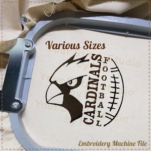May include: An embroidery hoop holding fabric with a brown design. The design features a cardinal bird head and the text "CARDINALS FOOTBALL". The text "Various Sizes" and "Embroidery Machine File" are also present.