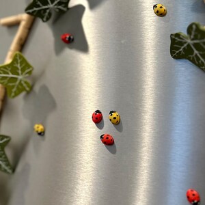 May include: A silver surface with a variety of red and yellow ladybug magnets. The ladybugs are arranged in a random pattern.