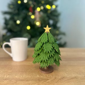 May include: A small green artificial Christmas tree with a gold star on top, sitting on a wooden table.