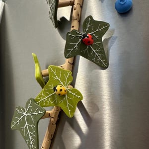 May include: A 3D printed ivy vine with green leaves and ladybugs. The vine is made of brown plastic and has a realistic look. The ladybugs are red with black spots.