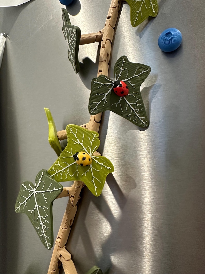 May include: A 3D printed ivy vine with green leaves and ladybugs. The vine is made of brown plastic and has a realistic look. The ladybugs are red with black spots.