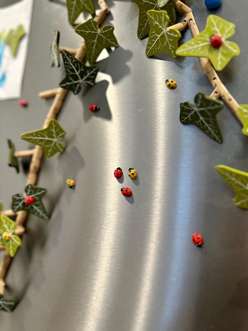 May include: A silver refrigerator with a decorative ivy vine and red and yellow ladybugs attached to it.