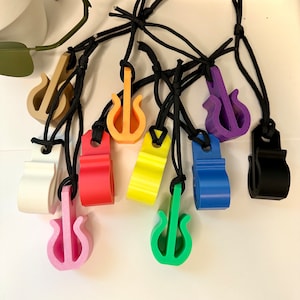 May include: A collection of colorful guitar-shaped pendants, each suspended from a black cord. The pendants come in various colors, including white, pink, red, yellow, green, blue, purple, and black. The guitar design is simple and stylized.