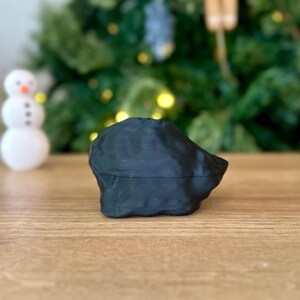 Op de afbeelding: Een zwart, 3D-geprint, abstract beeldhouwwerk met een glad, getextureerd oppervlak. Het beeldhouwwerk staat op een houten tafel.