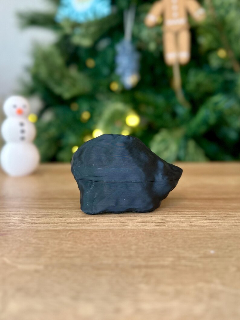 Op de afbeelding: Een zwart, 3D-geprint, abstract beeldhouwwerk met een glad, getextureerd oppervlak. Het beeldhouwwerk staat op een houten tafel.