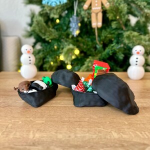 Op de afbeelding: Twee zwarte, rotsvormige dozen met open deksels. E&eacute;n doos bevat een klein knuffeldier en een gestreept speelgoed. De andere doos bevat kleurrijke verpakte snoepjes.