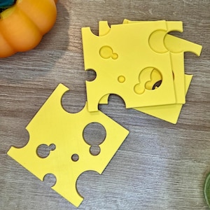 May include: Four yellow, square-shaped, cheese-shaped coasters with holes cut out. The coasters are stacked on top of each other.