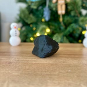 Op de afbeelding: Een zwart, onregelmatig gevormd, 3D-geprint object op een houten oppervlak.