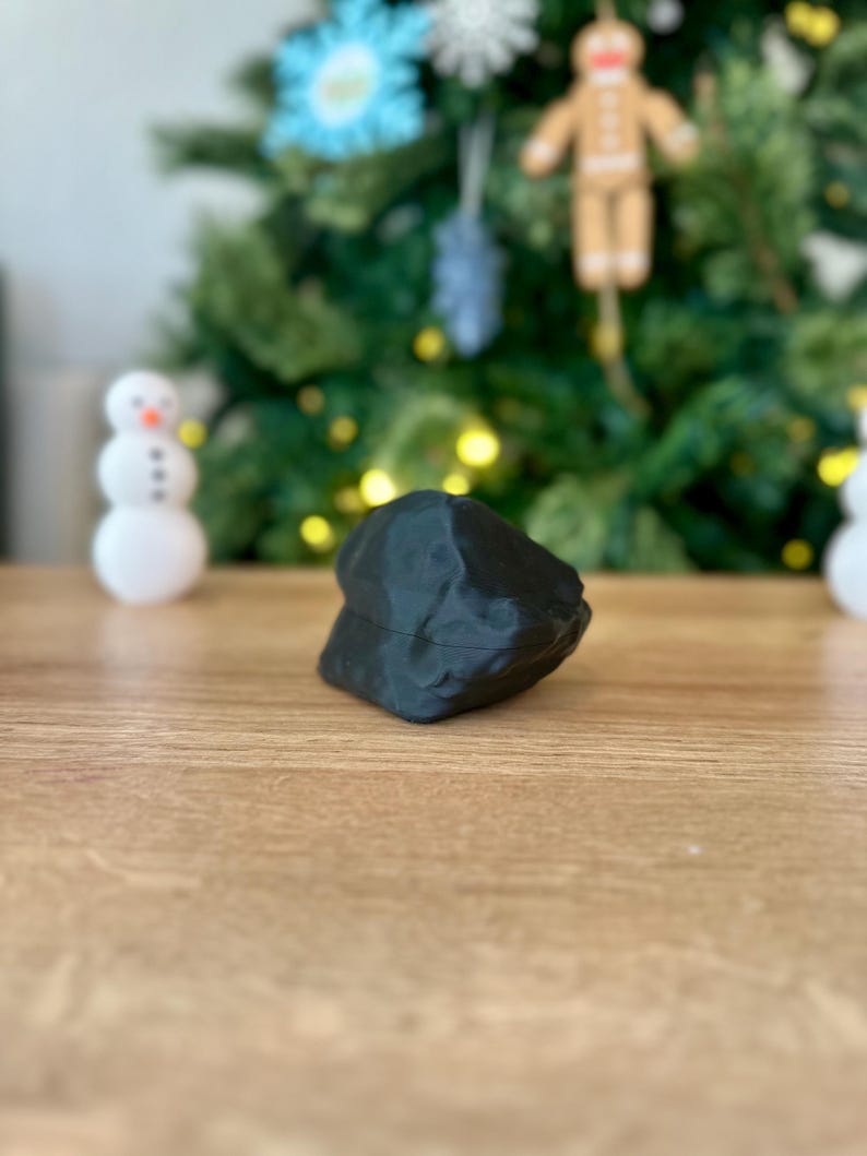 Op de afbeelding: Een zwart, onregelmatig gevormd, 3D-geprint object op een houten oppervlak.