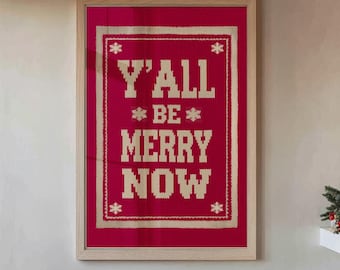 May include: A framed artwork with the text "Y'ALL BE MERRY NOW" in a pixelated font on a red background. The artwork is in a light wood frame and hangs on a white wall. A cactus is in a pot on the floor.