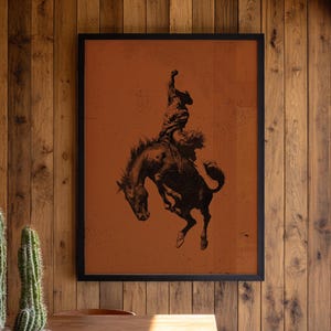 Cowboy bronc rider wall art on rust-orange background, vintage rodeo-inspired Western print.