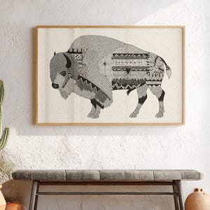 May include: A framed black and white illustration of a bison with intricate geometric patterns. The artwork is displayed on a white wall above a gray bench, with a cactus in a terracotta pot to the left and a decorative vase to the right.