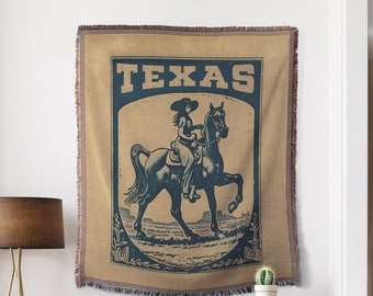 May include: A woven tapestry featuring a vintage illustration of a woman riding a horse with the word "TEXAS" printed in bold letters.