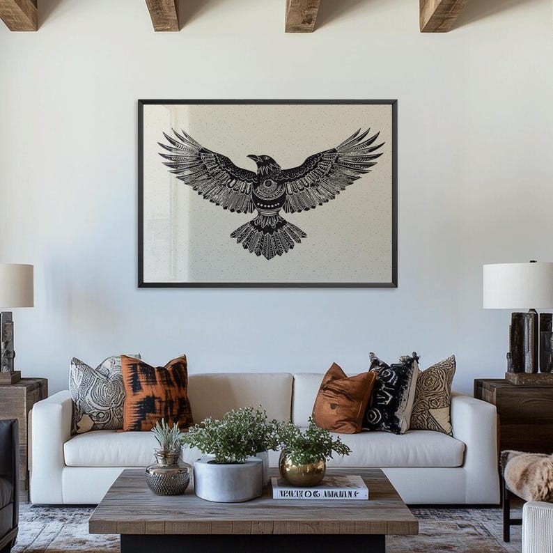 K&ouml;nnte beinhalten: Gerahmte Schwarz-Wei&szlig;-Illustration eines Raben mit ausgebreiteten Fl&uuml;geln. Das Kunstwerk wird &uuml;ber einem wei&szlig;en Sofa mit dekorativen Kissen gezeigt. Ein Holztisch mit Pflanzen und B&uuml;chern steht vor dem Sofa.