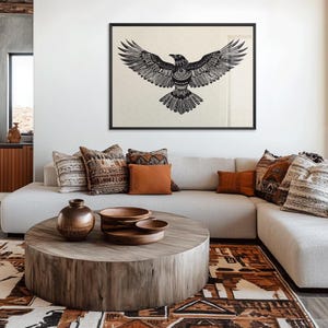 K&ouml;nnte beinhalten: Ein gerahmter Schwarz-Wei&szlig;-Kunstdruck eines Raben mit ausgebreiteten Fl&uuml;geln h&auml;ngt &uuml;ber einem hellfarbigen Ecksofa. Das Wohnzimmer verf&uuml;gt &uuml;ber einen Holztisch, dekorative Kissen und einen gemusterten Teppich, was eine gem&uuml;tliche, b&ouml;hmische &Auml;sthetik schafft.