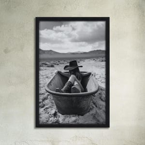 K&ouml;nnte beinhalten: Ein Schwarzwei&szlig;foto einer Person, die einen Cowboyhut und Stiefel tr&auml;gt und in einer Badewanne in einer W&uuml;stenlandschaft entspannt.