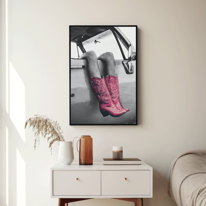 May include: A black and white photo of a person's legs wearing pink cowboy boots. The person is sitting in a car with their legs hanging out the window. The photo is framed in a black frame.