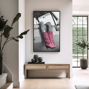 May include: Black and white photograph of a woman's legs wearing pink cowboy boots, hanging out of a car window.