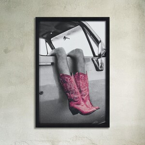 May include: A black and white photograph of a person's legs wearing pink cowboy boots sticking out of a car window.