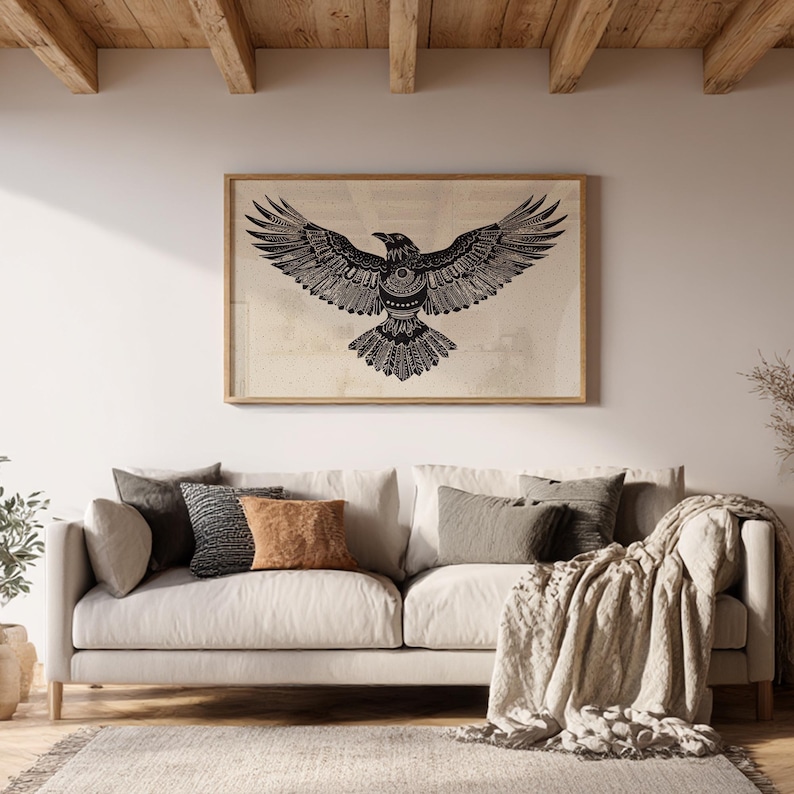 K&ouml;nnte beinhalten: Gerahmter Wandkunstdruck mit einer detaillierten schwarz-wei&szlig;en Illustration eines Raben mit ausgebreiteten Fl&uuml;geln. Das Kunstwerk wird &uuml;ber einem beigen Sofa mit dekorativen Kissen und einer Decke gezeigt.