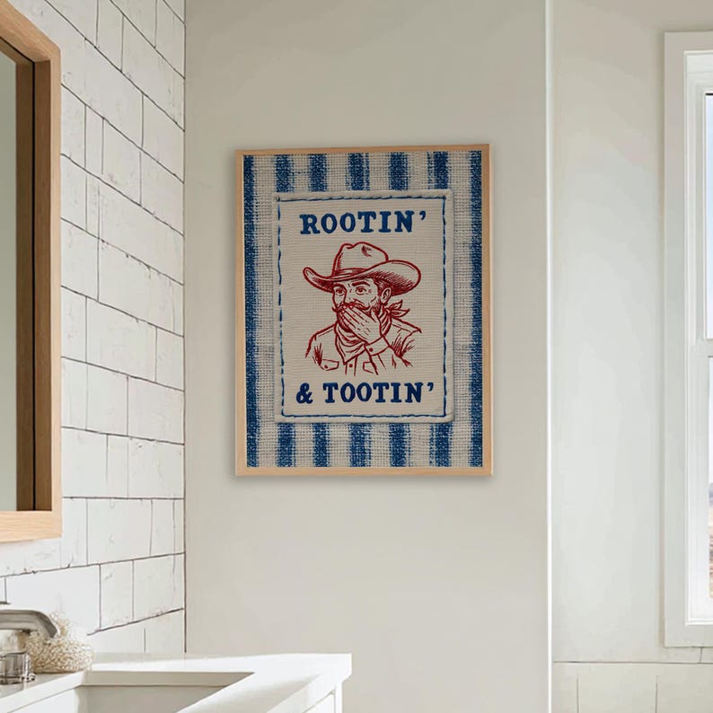 Może przedstawiać: Oprawiona grafika ścienna z ilustracją kowboja i napisem "ROOTIN' & TOOTIN'". Grafika ma niebiesko-białą obram&oacute;wkę w paski i beżowe tło. Kowboj ma na sobie kapelusz i zakrywa usta.