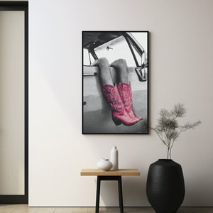 May include: Black and white photograph of a person's legs wearing pink cowboy boots sticking out of a car window.