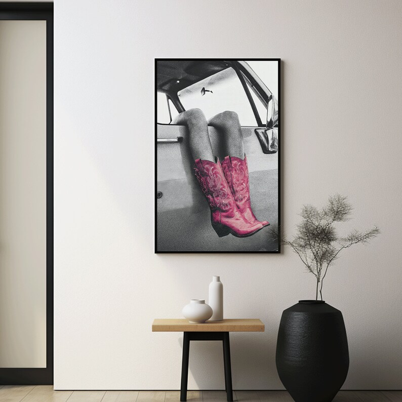May include: Black and white photograph of a person's legs wearing pink cowboy boots sticking out of a car window.