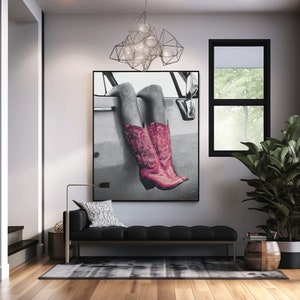 May include: A black and white photograph of a person's legs wearing pink cowboy boots. The photo is hanging on a wall in a living room with a black sofa, a plant, and a light fixture.
