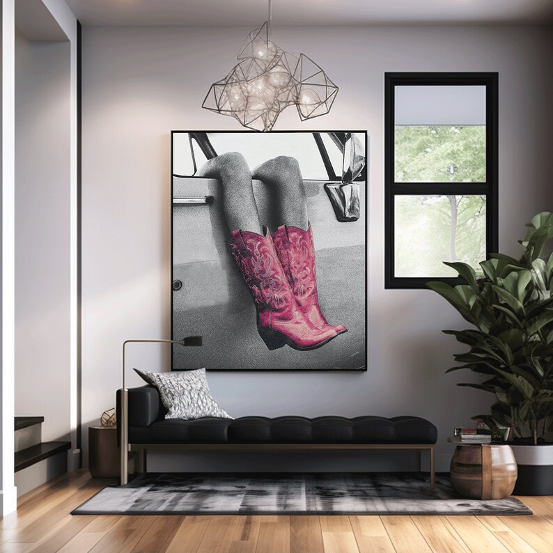 May include: A black and white photograph of a person's legs wearing pink cowboy boots. The photo is hanging on a wall in a living room with a black sofa, a plant, and a light fixture.