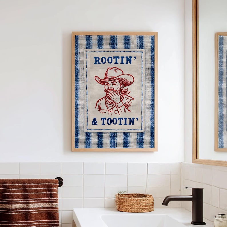 Może przedstawiać: Oprawiona grafika ścienna z ilustracją kowboja w czerwonym tuszu, z napisami "ROOTIN' & TOOTIN'". Grafika umieszczona jest na niebiesko-białym tle w paski, oprawiona w naturalne drewno. Element dekoracyjny do łazienki lub przestrzeni w stylu western.