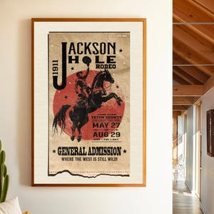 May include: Vintage poster advertising the Jackson Hole Rodeo in Teton County, Wyoming. The poster features a cowboy riding a bucking horse with a red, white, and blue color scheme. The dates of the rodeo are May 27th through August 29th. The text reads "Jackson Hole Rodeo, Teton County, Wyoming, May 27th - Aug 29th, General Admission, Where the West is Still Wild!"