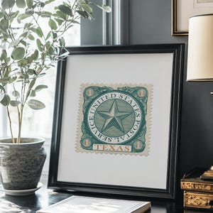 K&ouml;nnte beinhalten: Gerahmte Vintage-Briefmarkenkunst mit einer gr&uuml;n-wei&szlig;en Briefmarke mit Sterndesign. Die Briefmarke tr&auml;gt die Aufschrift "United States Postal Service Texas" und ist in einem schwarzen quadratischen Rahmen gerahmt. Das Kunstwerk wird auf einer schwarzen Oberfl&auml;che ausgestellt.