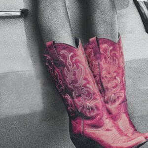 May include: A pair of pink cowboy boots with intricate floral embroidery. The boots are worn and have a distressed look.