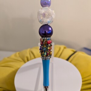 Turquoise blue bead pen with jewel-tone accents, two purple round beads and a fancy floral focal bead
