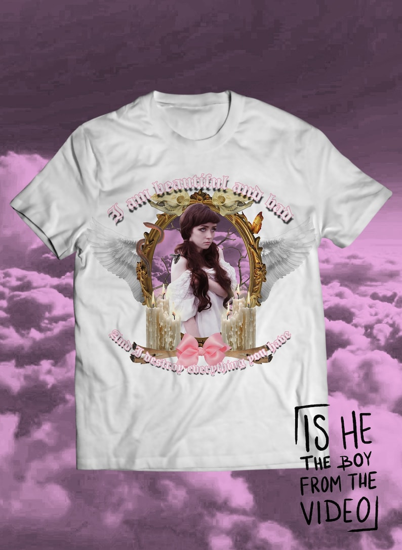 Peut inclure: T-shirt blanc avec un motif repr&eacute;sentant une fille en robe blanche avec un n&oelig;ud rose, entour&eacute;e de bougies et d'un cadre dor&eacute;. Le texte "I am beautiful and bad and I destroy everything you have" est imprim&eacute; sur le t-shirt. Le texte "IS HE THE BOY FROM THE VIDEO" est imprim&eacute; en bas du t-shirt.