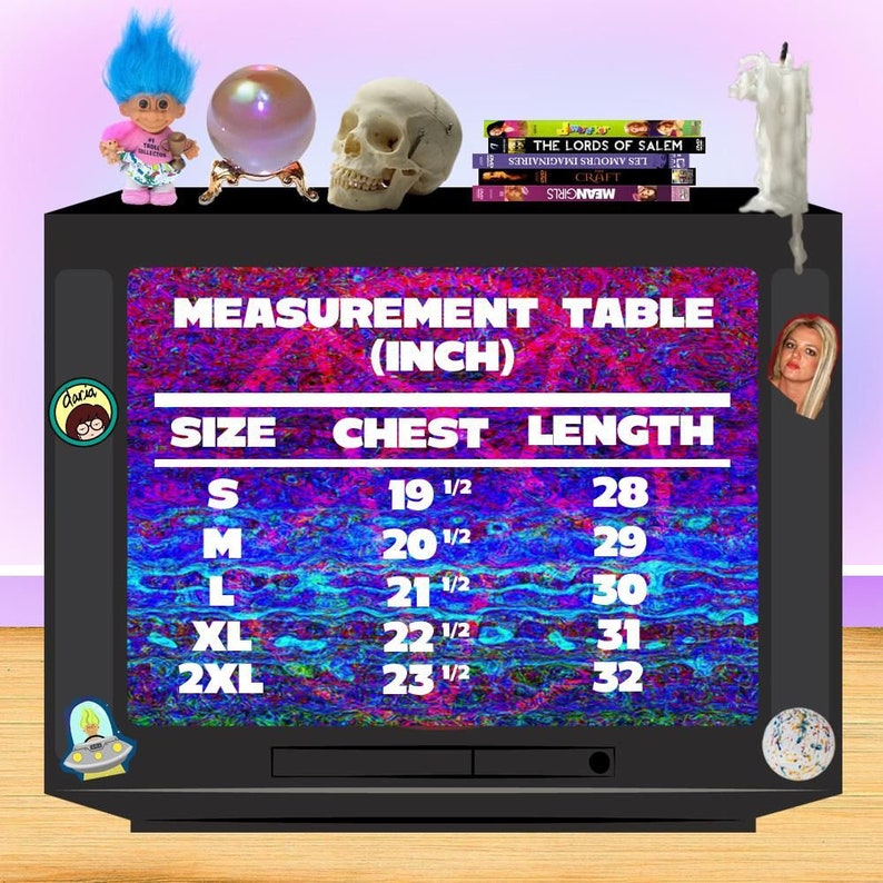 Peut inclure: Un &eacute;cran de t&eacute;l&eacute;vision vintage affichant un tableau des tailles pour les v&ecirc;tements. Le tableau montre les tailles S &agrave; 2XL avec les mesures de poitrine et de longueur correspondantes en pouces. L'&eacute;cran est entour&eacute; d'un cadre noir et est plac&eacute; sur un fond rose et bleu.