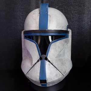 May include: A white and blue helmet with a black visor. The helmet has a weathered appearance with blue stripes and accents. The design is reminiscent of a science fiction or fantasy theme.