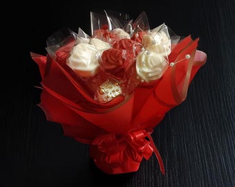 May include: A bouquet of chocolate roses in a red paper wrapper. The roses are white and red and are arranged in a circular pattern. The bouquet is tied with a red ribbon.