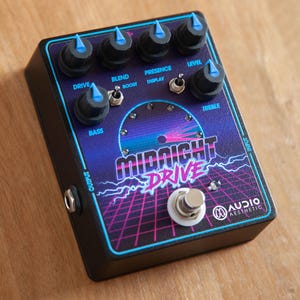 Könnte beinhalten: Ein schwarzes Gitarreneffektpedal mit blauem und violettem Design. Das Pedal hat ein großes Zifferblatt mit dem Text "MIDNIGHT DRIVE" und einen Fußschalter. Das Pedal hat Knöpfe mit den Beschriftungen "Drive", "Blend", "Presence", "Level", "Bass" und "Treble".