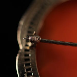 May include: Close-up of a silver brooch with a red cameo and a pin marked "14K".